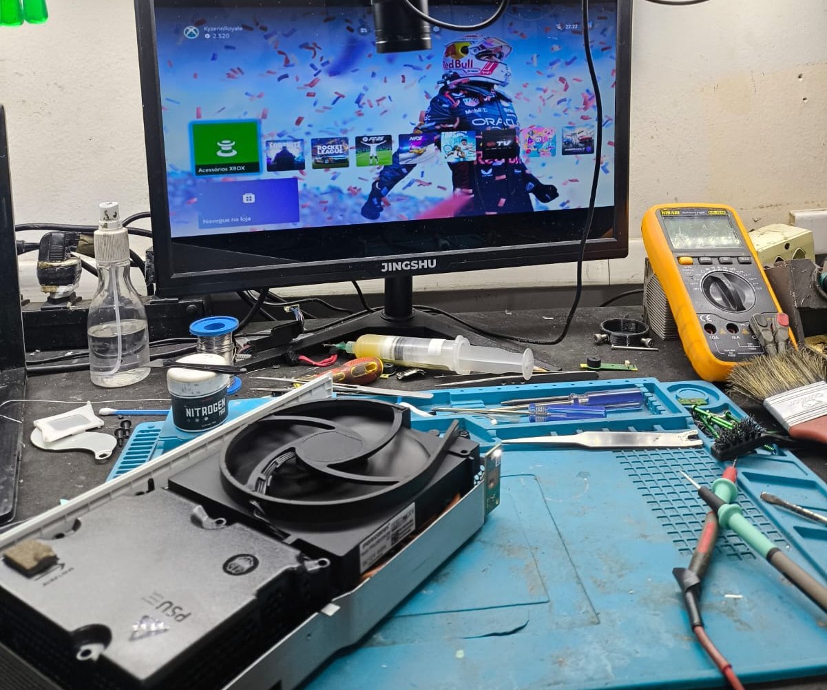 Bancada técnica da Games Pro com um Xbox Series S aberto sobre tapete azul, multímetro, ferramentas e monitor exibindo o painel do Xbox