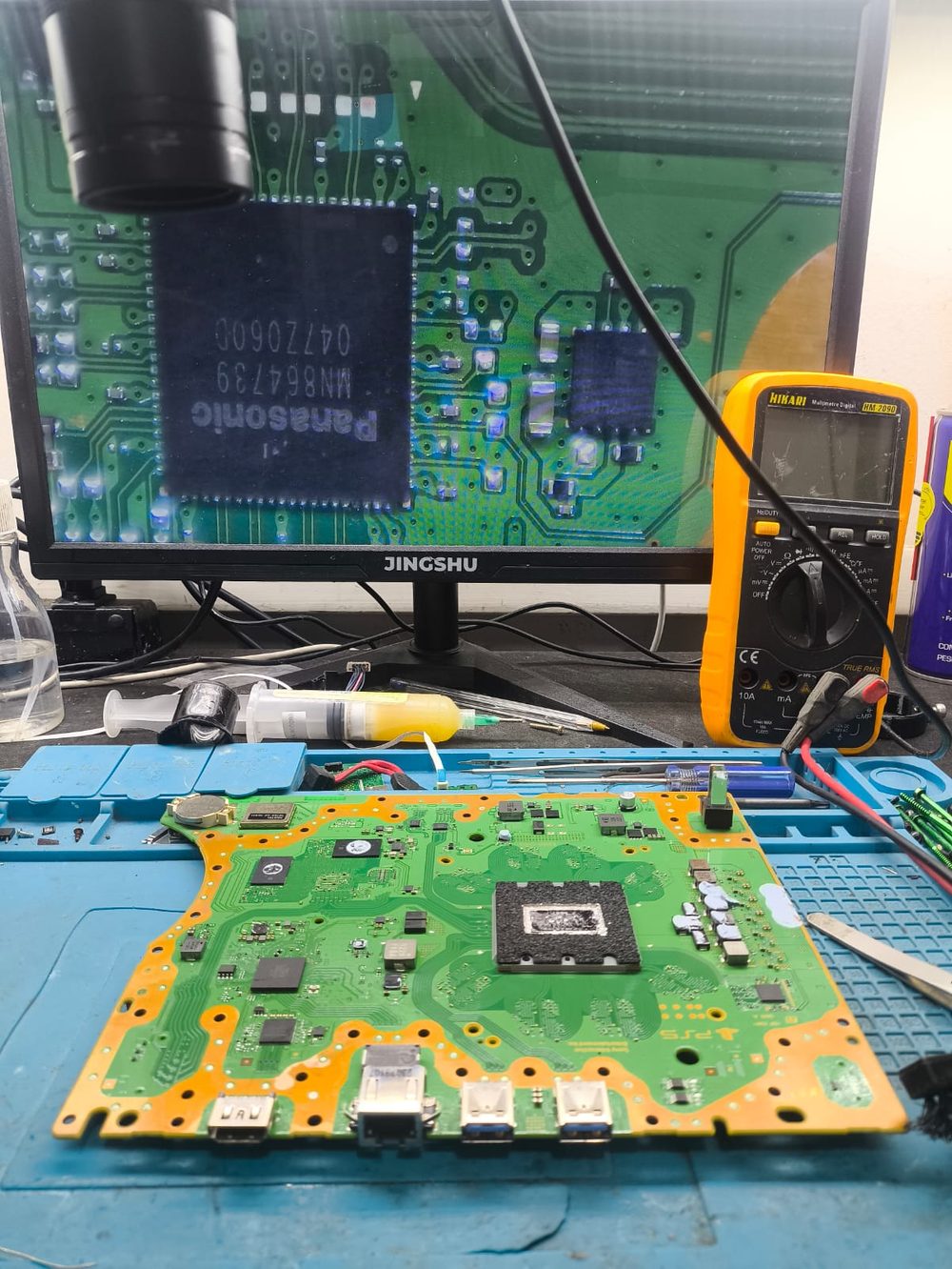 Placa de PlayStation 5 aberta na bancada com o CI HDMI ampliado no monitor do microscópio